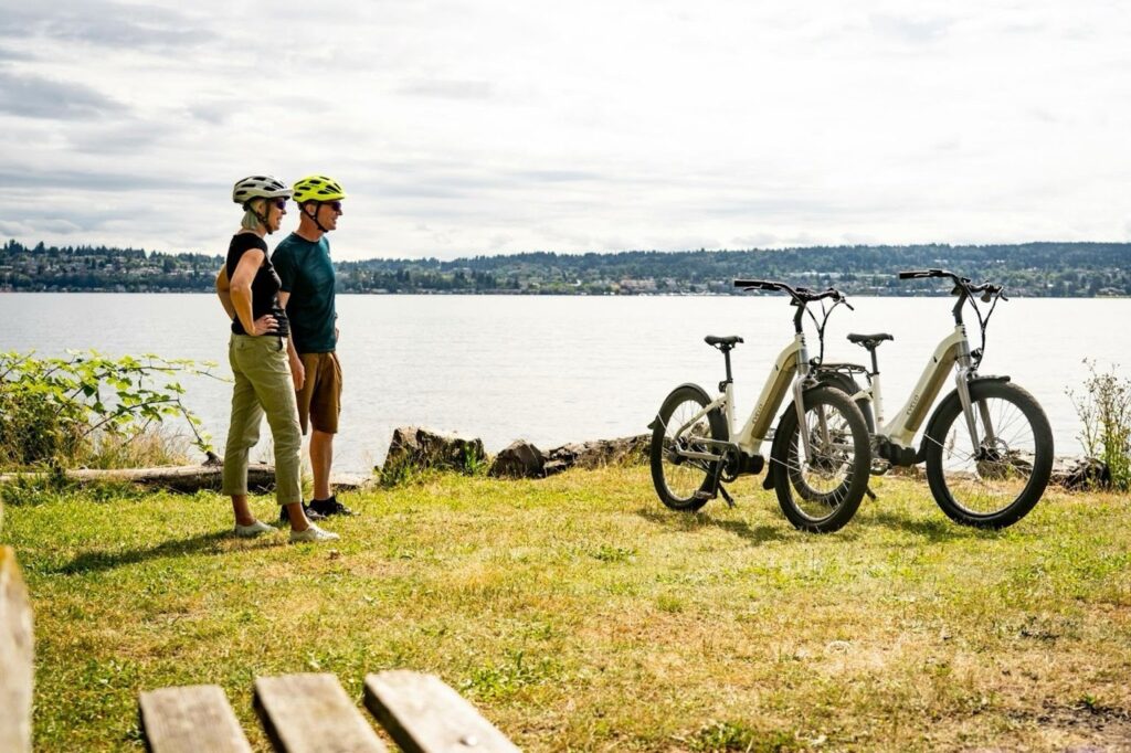 Older couple standing beside electric bikes near water