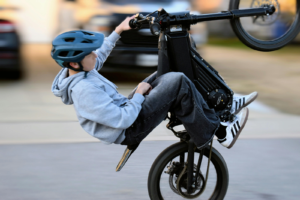Teen riding an electric bike doing a wheelie on a street without proper safety control