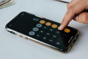 A close-up of a person's finger pressing the number five on a smartphone calculator app to perform a data-driven analysis.