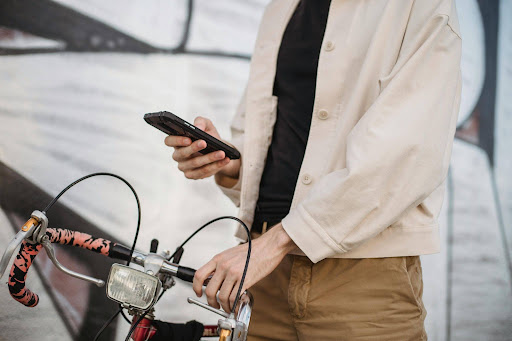 A cyclist standing next to a vintage road bike, holding a smartphone to file a incident report or contact local police.