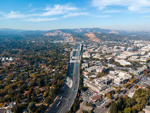An aerial high-angle view showing a multi-lane highway corridor running through suburban commercial and residential developments.