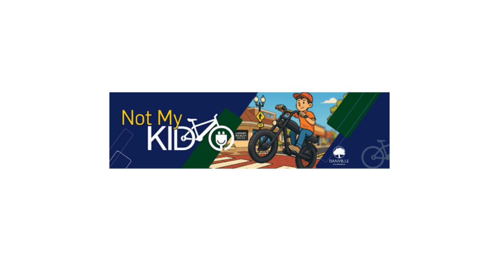 Town of Danville "Not My Kid" campaign banner showing a cartoon boy riding a black e-bike across a red crosswalk near downtown buildings.